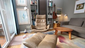 Un salon comprenant un fauteuil en cuir, un canapé, une table basse, une bibliothèque et une guitare.
