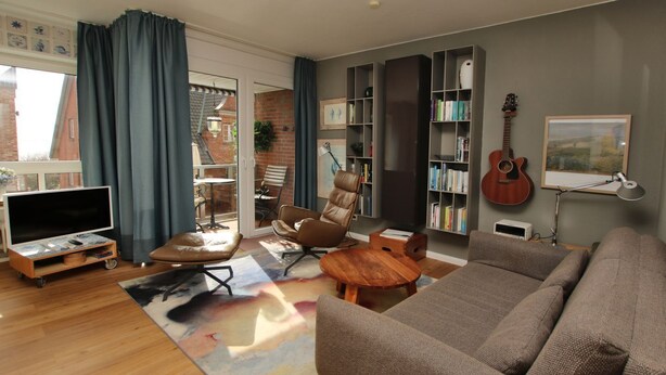 Un salon avec un canapé, une table basse, un tél éviseur posé sur un meuble, une bibliothèque et une guitare.