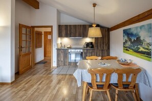 A cozy kitchen with wooden cabinets, a dining table with chairs, and a painting of mountains on the wall.
