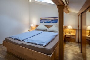 A bedroom with a wooden bed, two bedside tables with lamps, a painting on the wall, and a wooden floor.