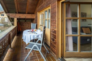 A wooden cabin with a balcony, a dining table with chairs, and a sliding glass door leading to a living area.