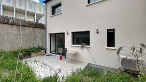 A modern building with a flat roof, a small patio area with a table and chairs, and a large sliding glass door.