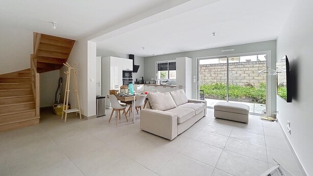 A modern living space with a staircase, a dining area, a sofa, and a kitchen.