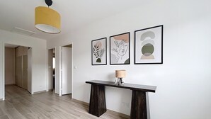 A hallway with a wooden floor, a dark console table with a lamp, and three framed artworks on the wall.