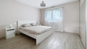 A modern bedroom with a large bed, bedside tables, a ceiling light, and a window with curtains.