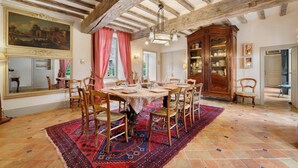 A dining room with a large table, chairs, a patterned rug, and a wooden cabinet.