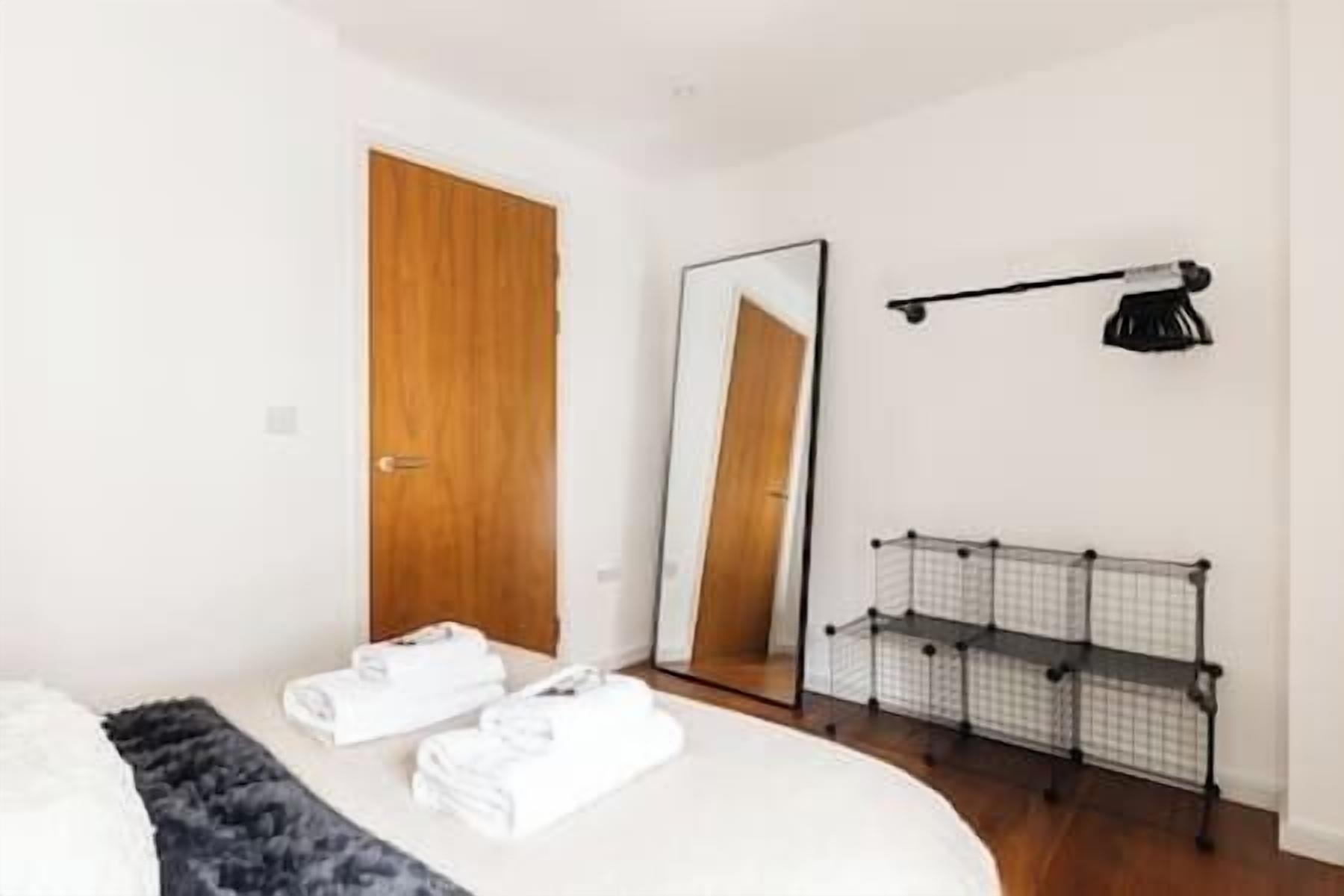 Un dormitorio con cama, puerta de madera, espejo y perchero.