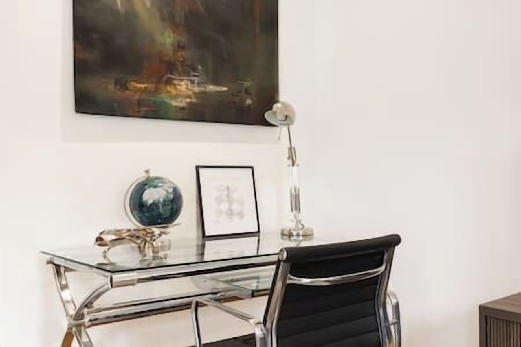 A modern office space with a glass desk, a black office chair, a globe, and a framed picture on the wall.
