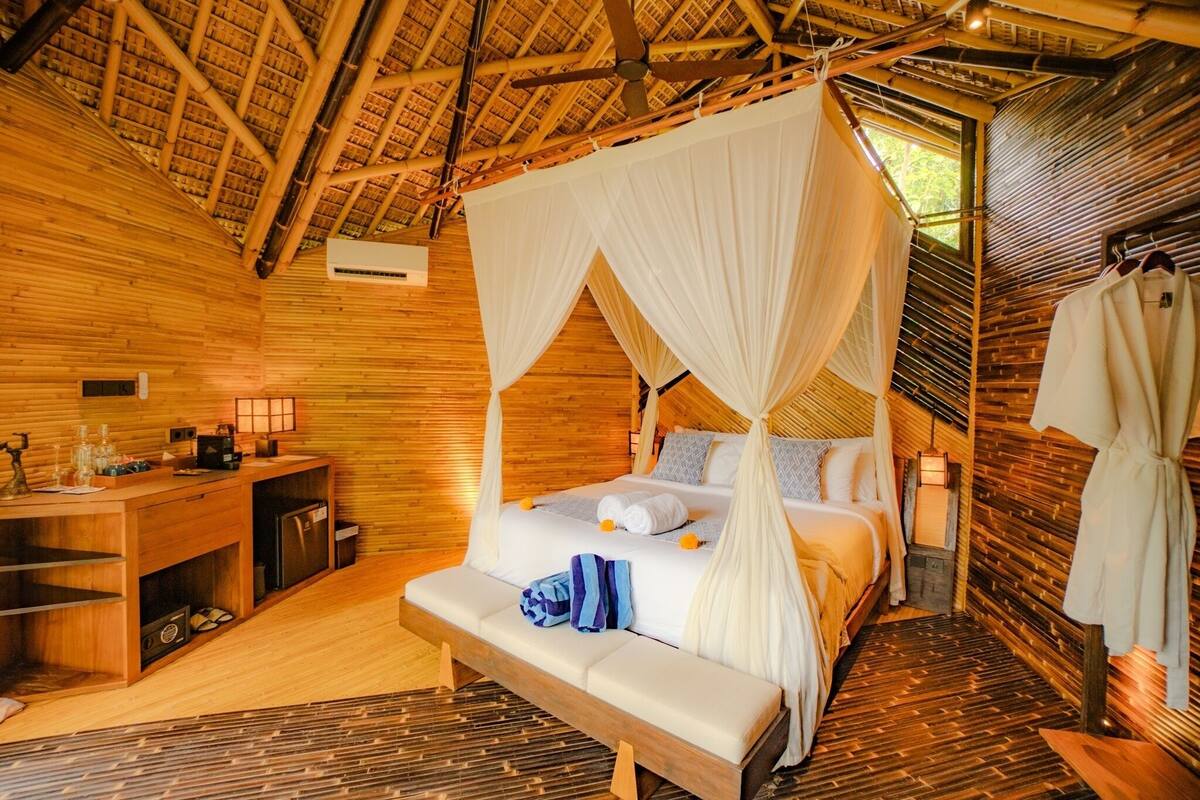 A room with a bed under a canopy, a bedside table, a bench, and a hanging robe.