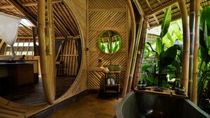 Habitación de estilo bambú con una bañera grande, un espejo redondo y una mesa de madera con artículos de aseo.