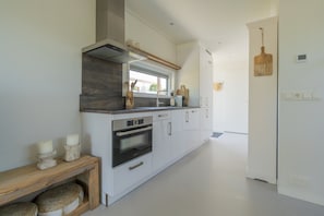 Une cuisine moderne avec des meubles blancs, un four encastré et une fenêtre au-dessus de l’évier.