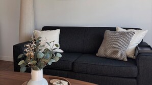 Ein modernes Wohnzimmer mit einem dunkelgrauen Sofa, einer weißen Vase mit Blumen und zwei abstrakten Kunstwerken an der Wand.