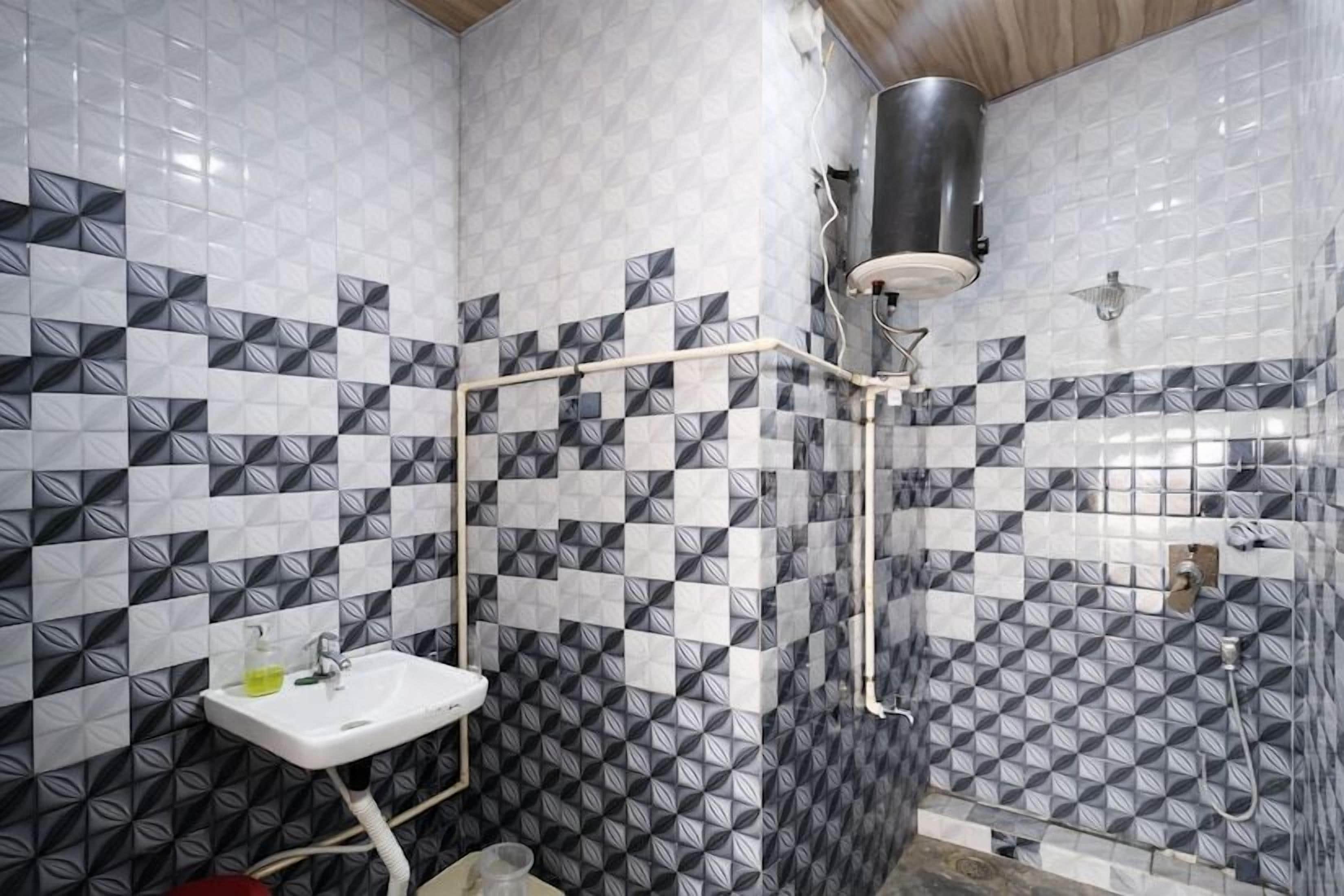 A bathroom with a white sink, a shower with a black hose, and patterned tiles on the walls.