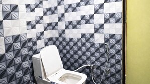 A bathroom with a toilet, a shower, and a tiled wall with a geometric pattern. - The Golden Wings Hotel  (Dewas)