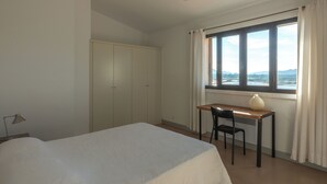 A bedroom with a bed, a desk, a chair, a wardrobe, and a window with a view.