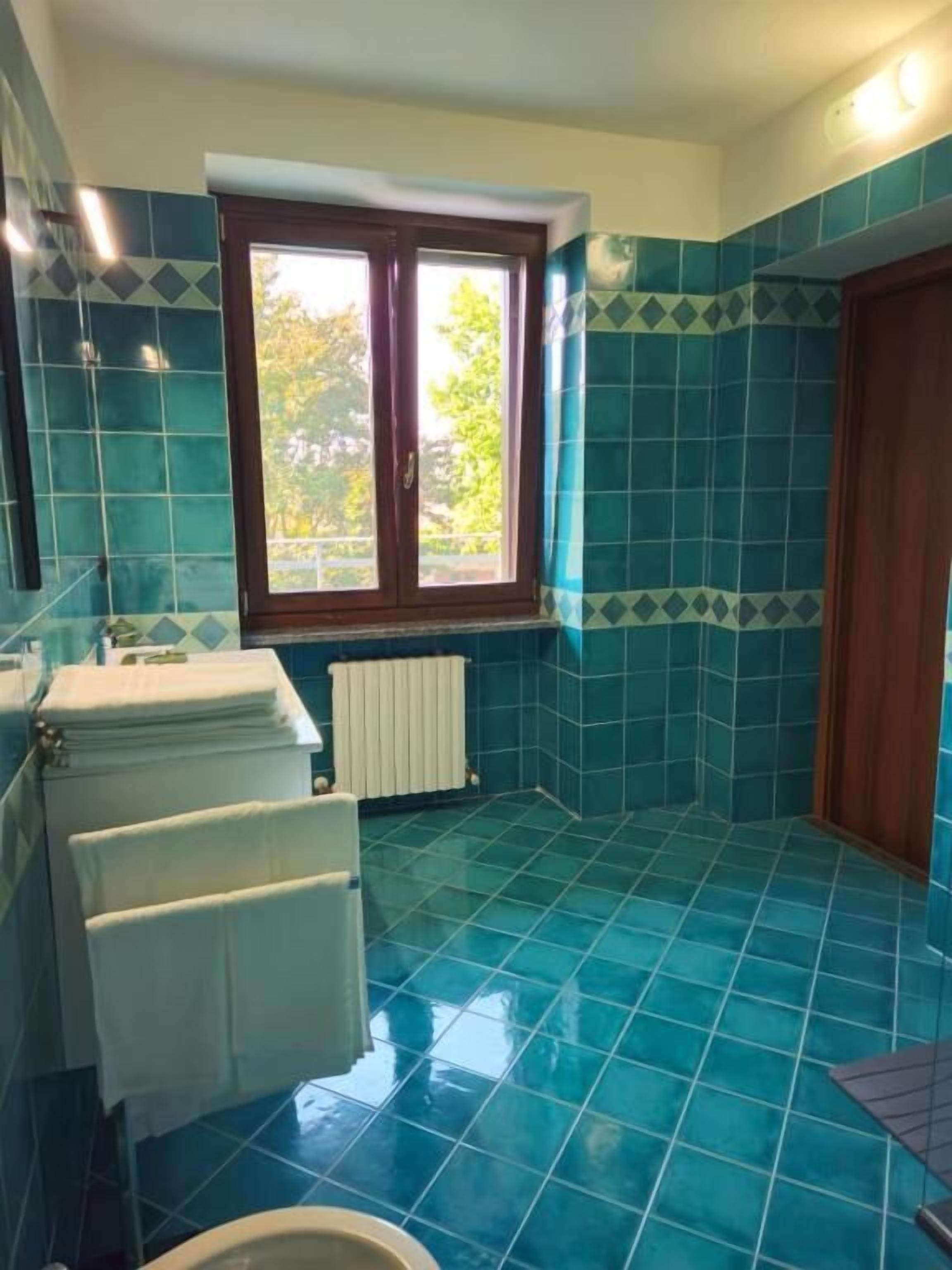 A bathroom with blue tiles, a window, a radiator, and a wooden door.