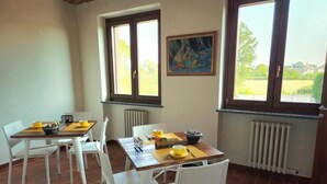 A dining area with a table set for four, white chairs, and a window with a view of greenery. - B&B Cascina del Gelso (Santena)