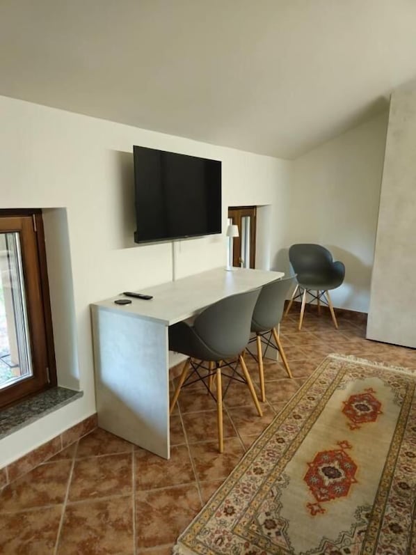Una sala moderna con un televisor de pantalla plana montado en la pared, una mesa de comedor con cuatro sillas y un tapete estampado en el suelo.