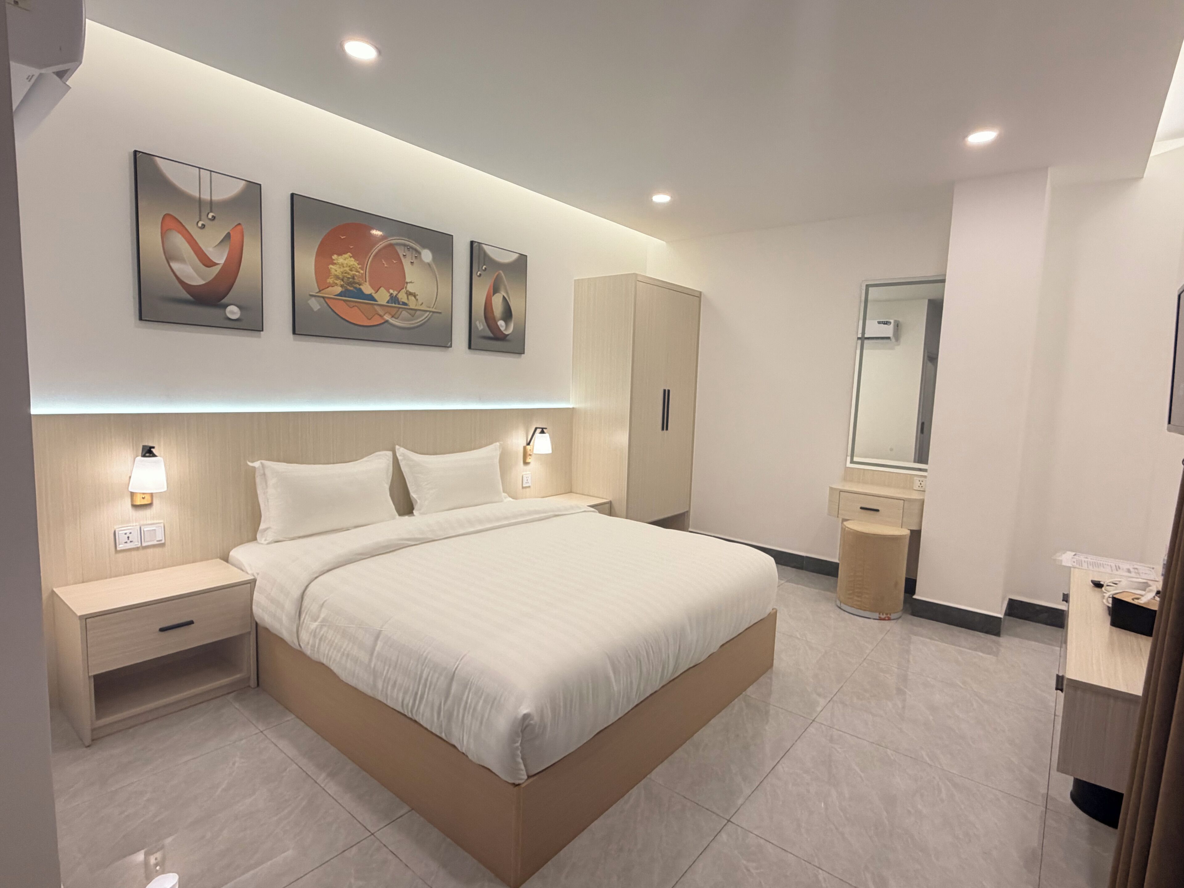 Ein modernes Hotelzimmer mit einem großen Bett, Nachttischen, einem Kleiderschrank, einem Spiegel und Bildern an der Wand.