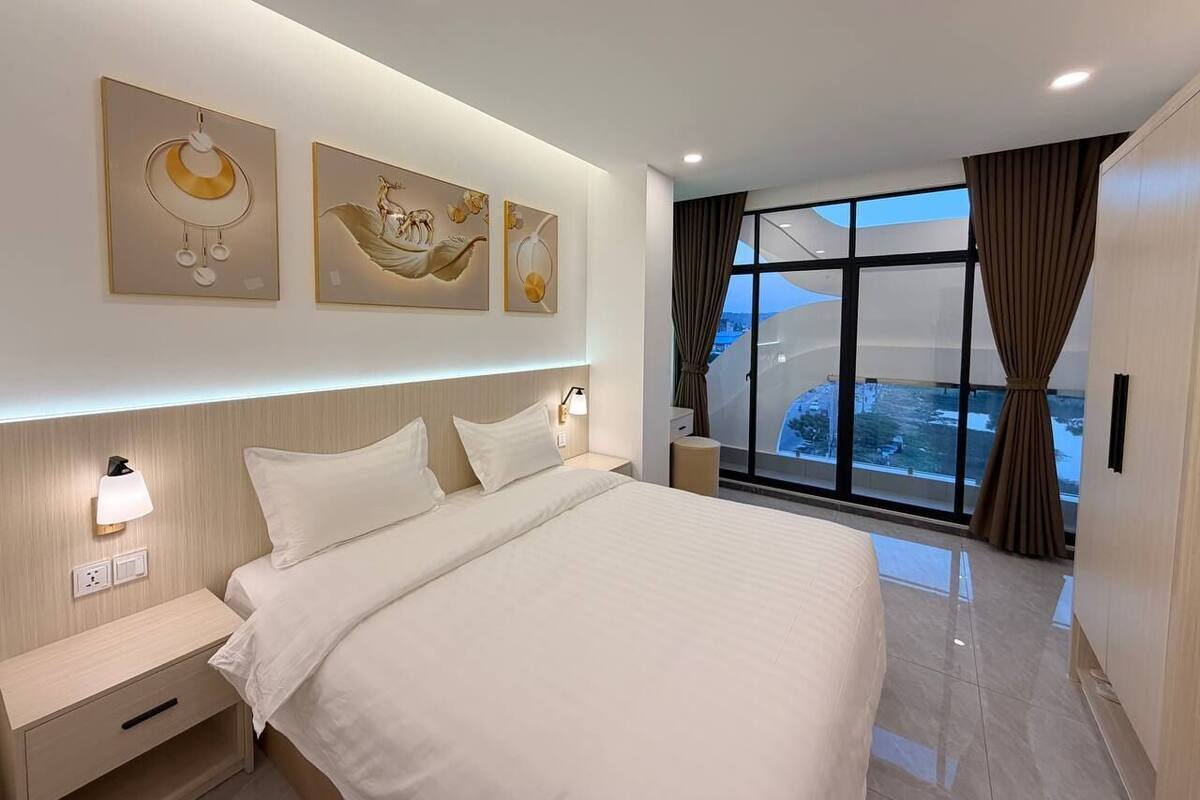 A modern hotel room with a large bed, a nightstand, a wall-mounted lamp, and artwork above the bed.