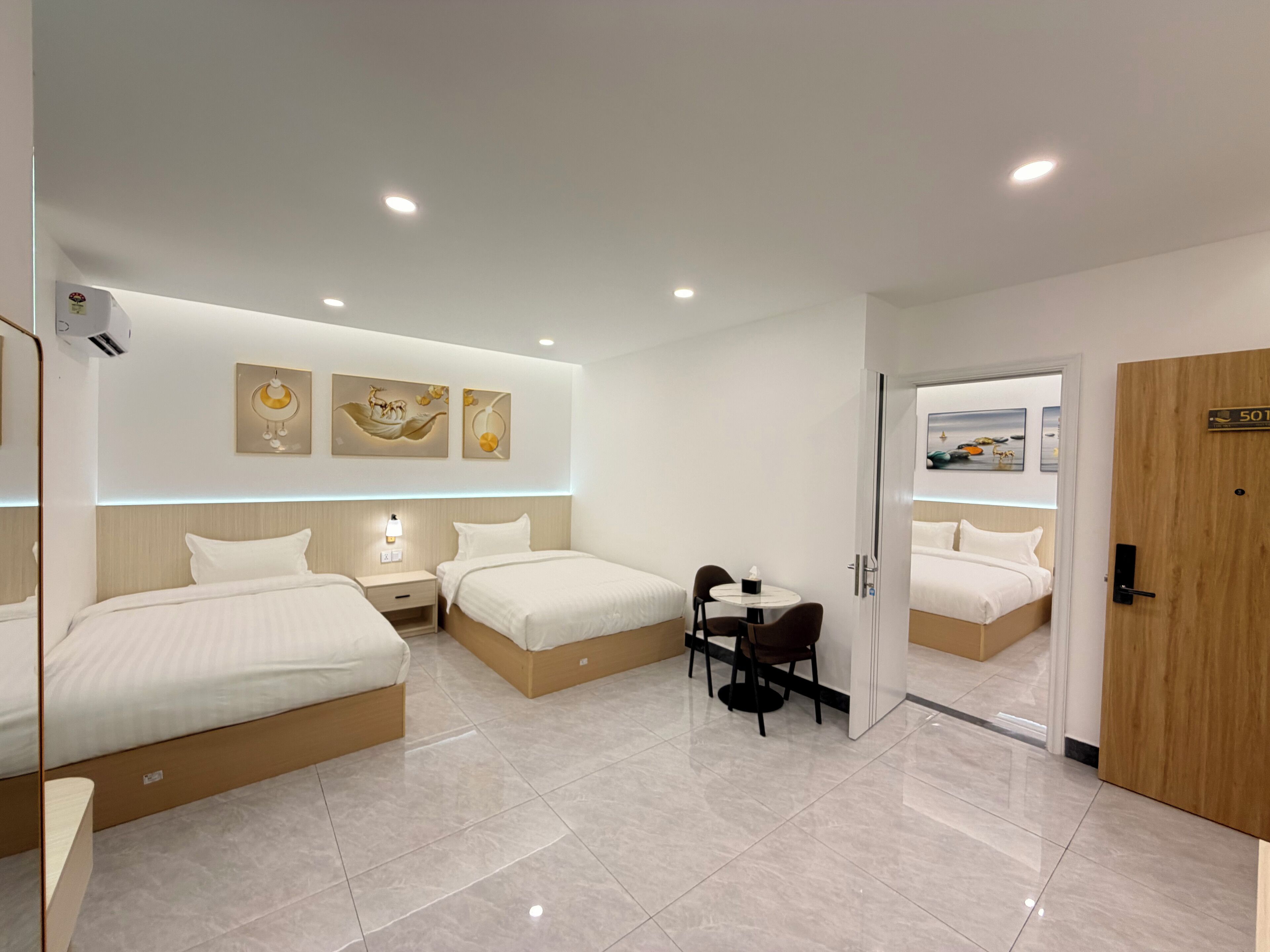 Una habitación de hotel moderna con dos camas, una mesita con una silla y cuadros en la pared.