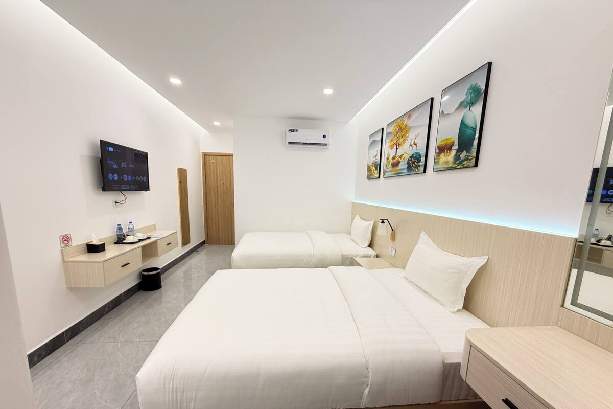 A modern hotel room with two beds, a TV, a desk, and a bathroom.