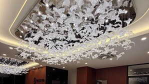 A modern lobby with a large white sofa, a reception desk, and a unique ceiling light fixture. - The Sky Plus (Sihanoukville)