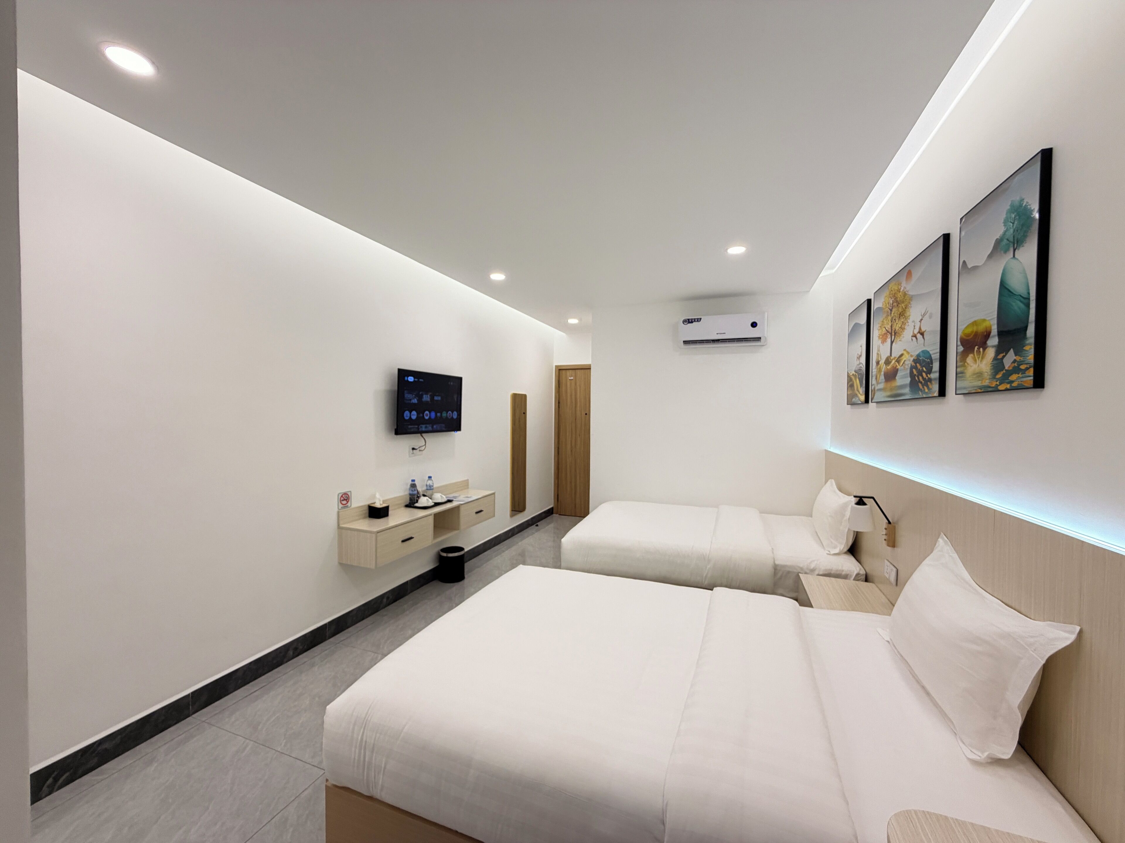 A modern hotel room with two beds, a TV, a minibar, and artwork on the wall.
