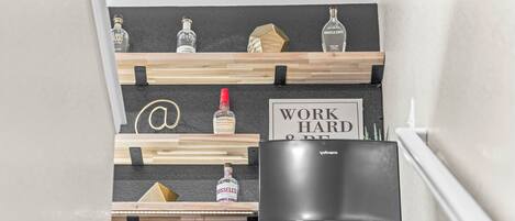 A kitchen with a black refrigerator, wooden shelves holding bottles, and a sign that reads "WORK HARD & BE KIND".