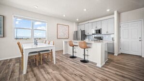 Een moderne keuken met witte kasten, een centraal eiland met krukken, en een eethoek met tafel en stoelen.