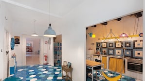Eine moderne Küche mit blau-weißen, sechseckigen Fliesen, einer hängenden, gelben Hängematte und einem Essbereich mit Tisch und Stühlen.