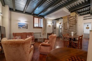 A spacious living area with a high ceiling, a wooden staircase, and a dining table. - GuestHost - Palazzo Costaguti in the heart of Rome (Rome)