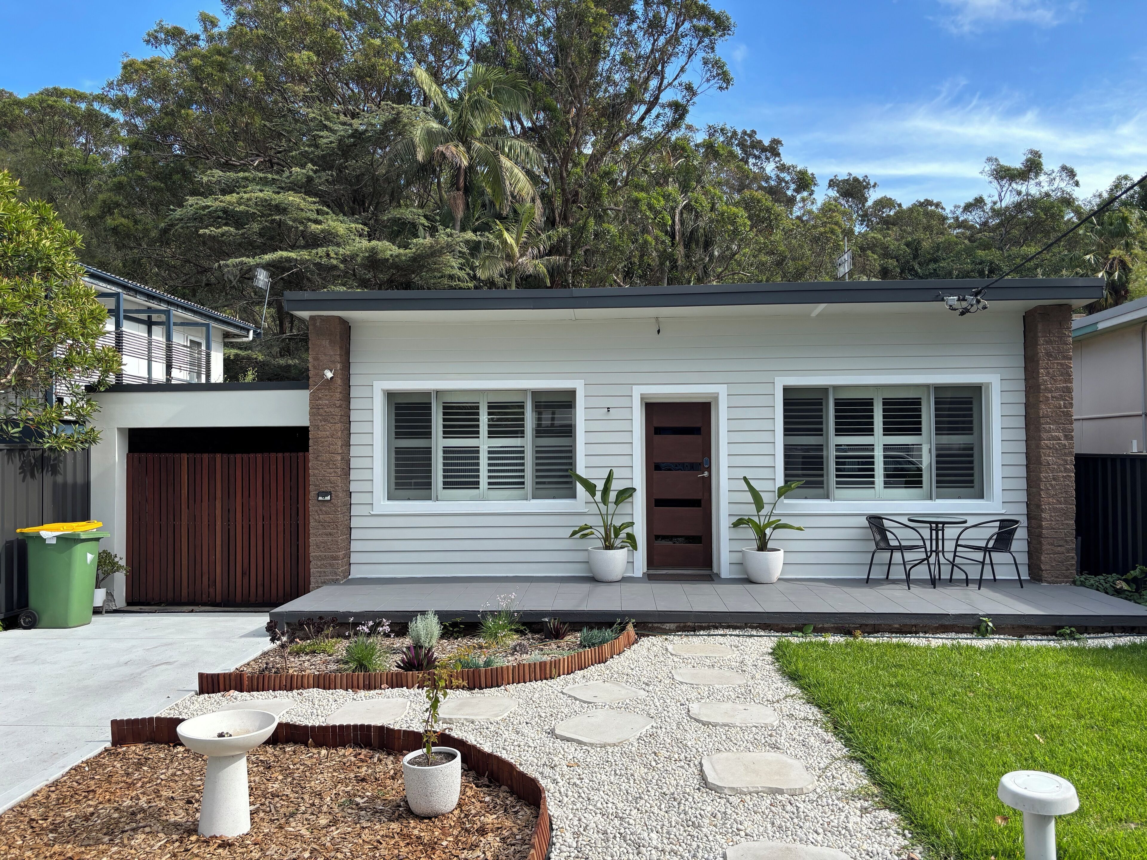 A modern two-story house with a front porch, a brown door, and two windows with shutters.