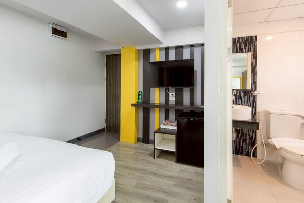 A hotel room with a bed, a desk, a chair, a small shelf, a mirror, and a toilet. - Riski Residence Bangbuathong (Bang Bua Thong)