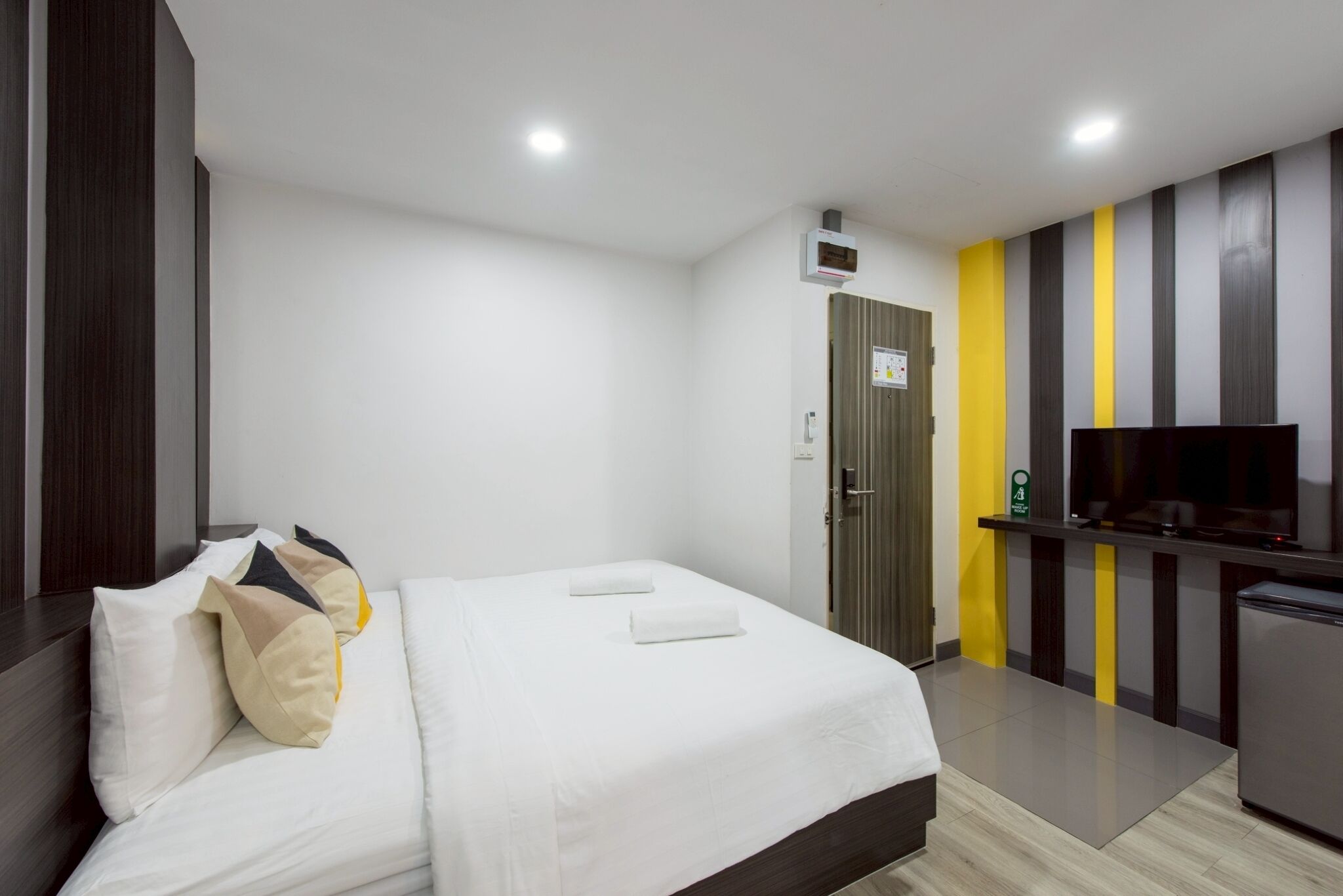Habitación de hotel con cama, televisor, refrigerador pequeño y una puerta con un letrero.