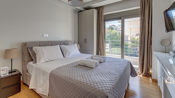 Una camera da letto moderna con un letto grande, un comodino con una lampada, una cassettiera e una TV montata a parete.