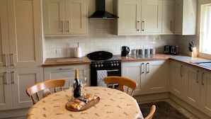 A kitchen with light-colored cabinets, a black stove, and a dining table set with a bottle of wine and bread.