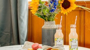 A table with a floral arrangement, two bottles of lavender lemonade, macarons, and a plate of nuts. - Gateway Suites: Perfect rest on your way to Banff! (Harvie Heights)