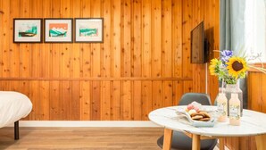 A hotel room with a wooden paneled wall, a bed, a dining table with breakfast items, and three framed pictures. - Gateway Suites: Perfect rest on your way to Banff! (Harvie Heights)