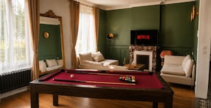 A pool table in a room with a fireplace, a sofa, and a television displaying 'NETFLIX'.