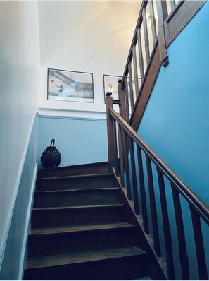 A staircase with wooden steps and a metal railing, leading to a landing with two framed pictures.
