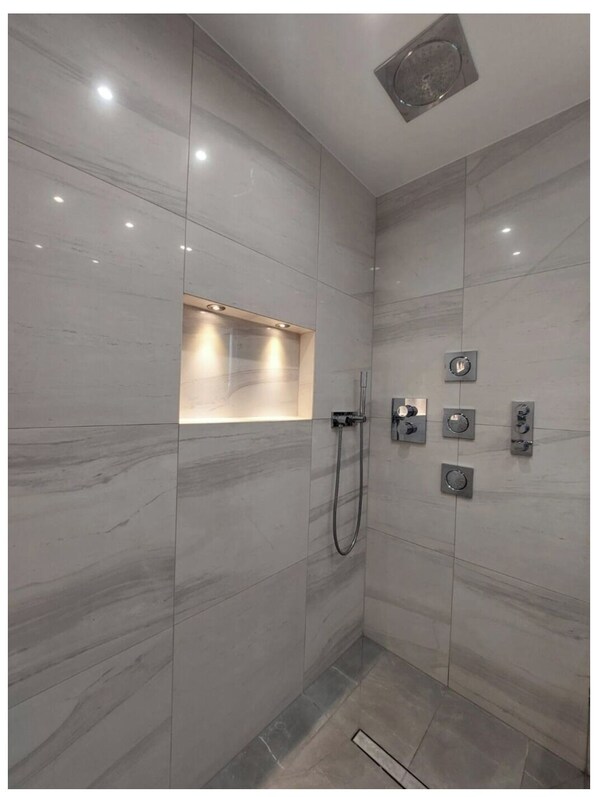 Ein modernes Badezimmer mit Marmorwänden, einer integrierten Dusche und einer Wandarmatur.