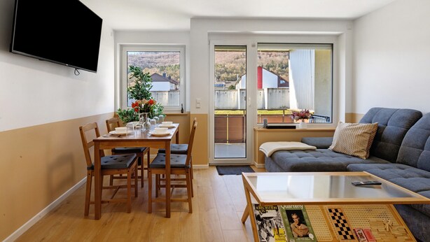 Uma sala de estar com televisão de tela plana, uma mesa de jantar com cadeiras, um sofá e uma mesa de centro.