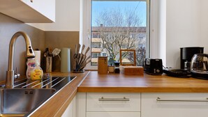 Cozinha moderna com pia de aço inoxidável, bancada de madeira e vista para o exterior através de uma porta de vidro.