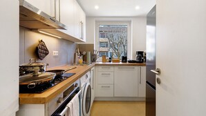 Uma cozinha compacta com fogão, forno e máquina de lavar, bancadas de madeira e armários brancos.