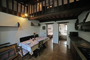 A dining area with a table set for two, wooden beams on the ceiling, and a kitchen area with a stove.