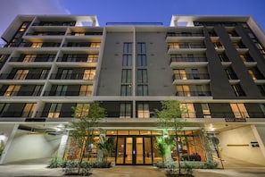 A multi-story hotel with a central entrance, balconies, and a guest garage. - Brand New Hotel | 1 Bedroom Suite w/Balcony + Rooftop Pool | Luxe Edgewater Stay (Miami)