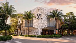 Een modern gebouw met een opvallend 'LV' logo, omringd door palmbomen en begroeiing.