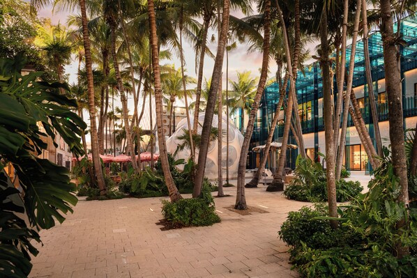 A courtyard with palm trees, a glass building, and a brick pathway.