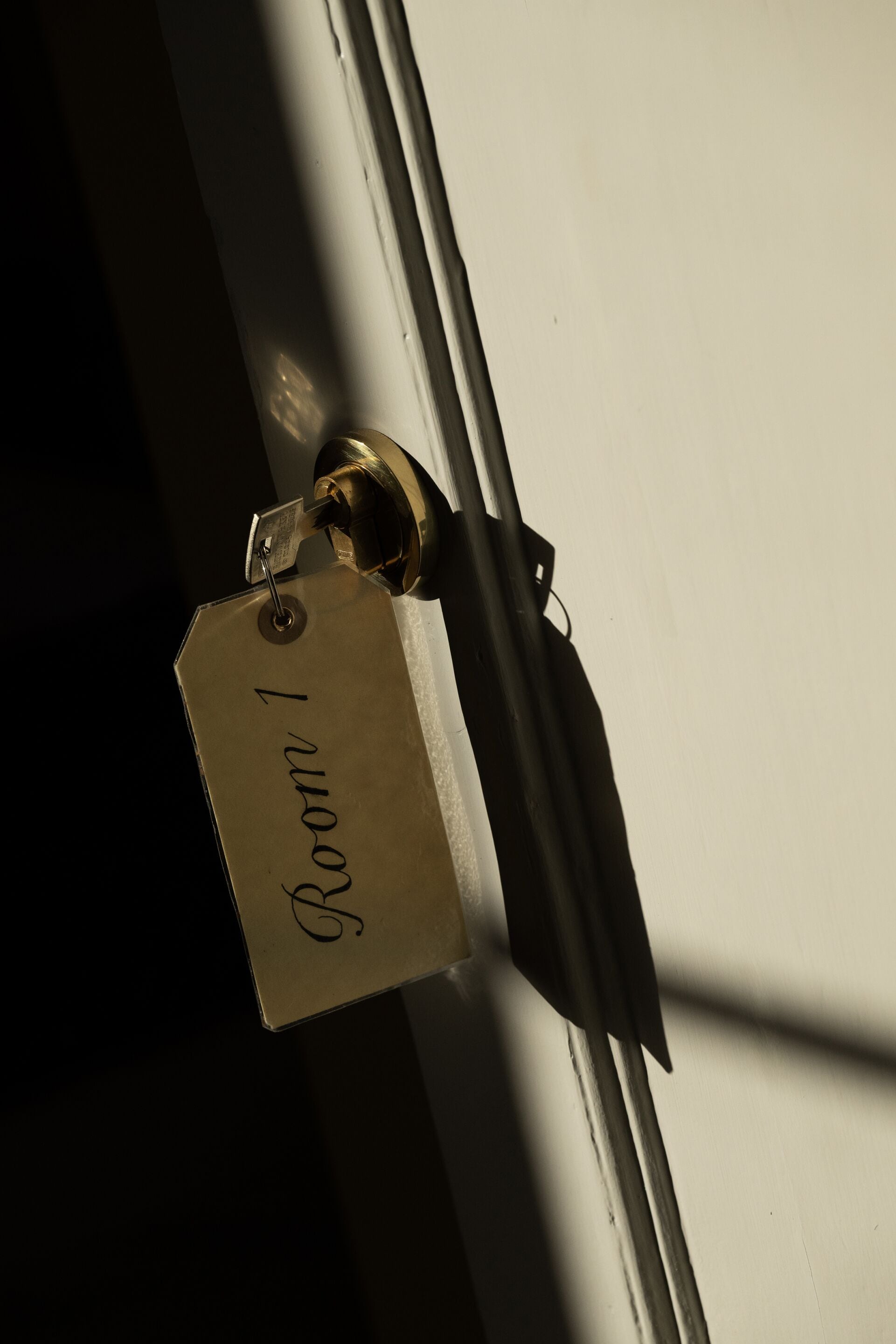 Een messing sleutelhanger met de tekst 'Room 1' gegraveerd, bevestigd aan een deurklink.